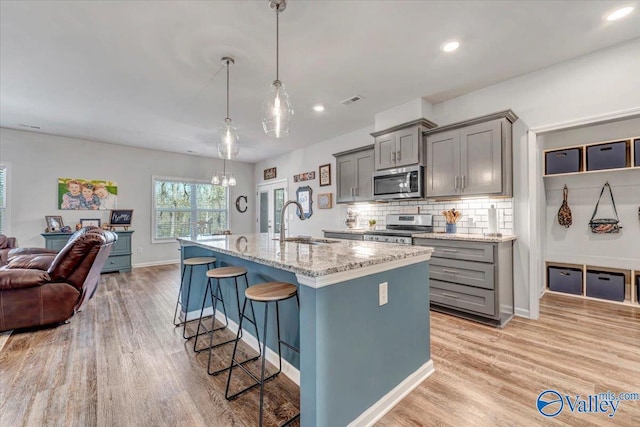 kitchen featuring appliances with stainless steel finishes, decorative light fixtures, a kitchen bar, light stone counters, and a center island with sink