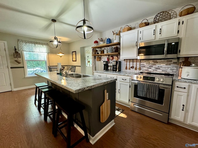 kitchen with decorative light fixtures, a kitchen island with sink, dark wood-type flooring, white cabinetry, and stainless steel appliances