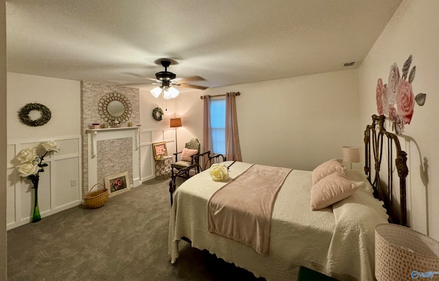 bedroom with dark carpet, ceiling fan, a fireplace, and a textured ceiling