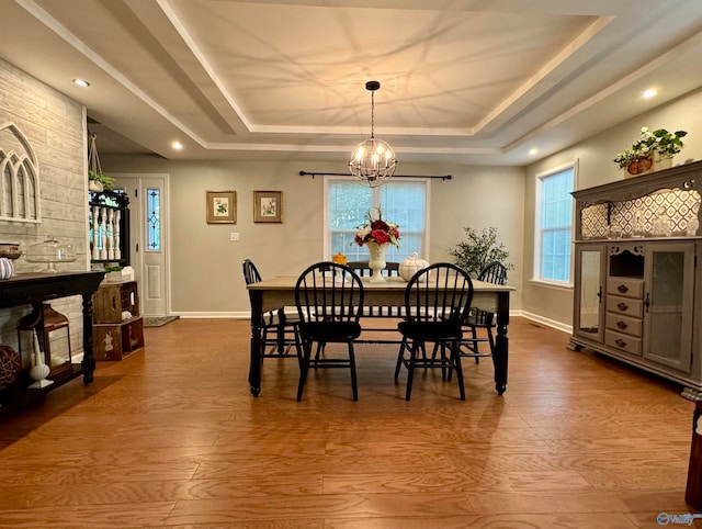 dining space with wood-type flooring, an inviting chandelier, and a tray ceiling