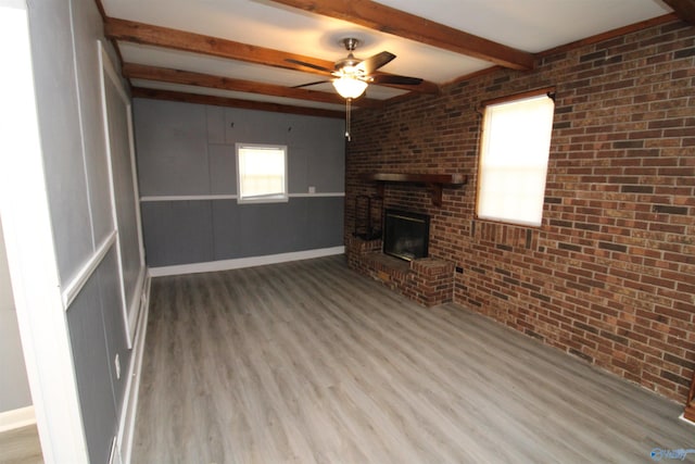 unfurnished living room featuring a brick fireplace, beam ceiling, hardwood / wood-style flooring, ceiling fan, and brick wall