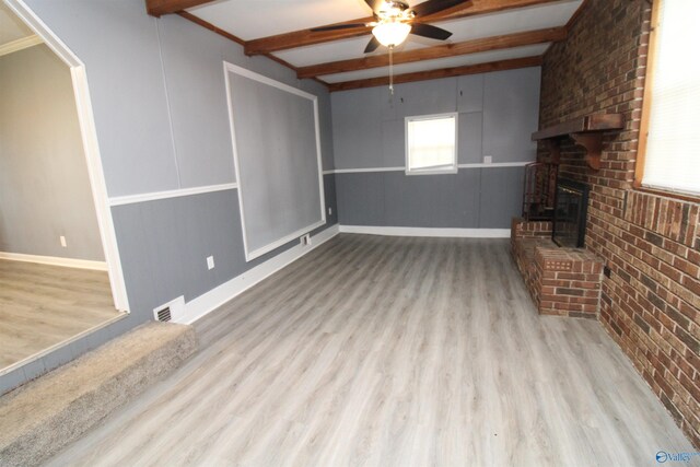 unfurnished living room with beam ceiling, light hardwood / wood-style floors, brick wall, a fireplace, and ceiling fan