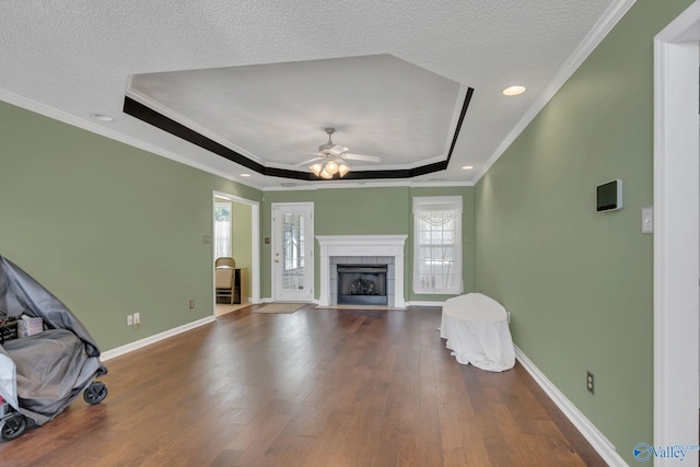 living area featuring a wealth of natural light, a tray ceiling, a tiled fireplace, and wood finished floors