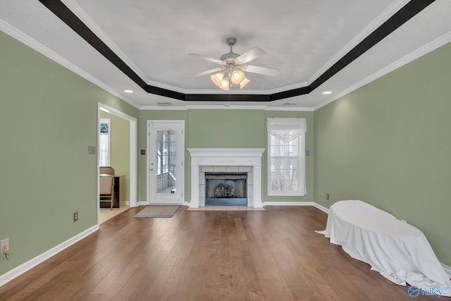 unfurnished living room with a tray ceiling, crown molding, baseboards, and wood finished floors