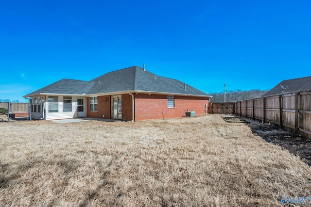 rear view of house featuring a fenced backyard, central AC unit, a lawn, and brick siding