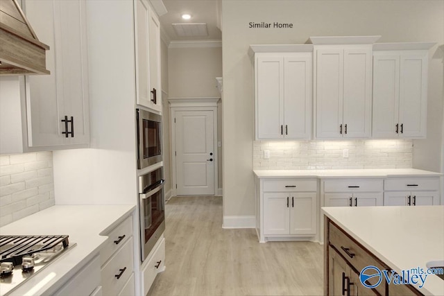 kitchen with appliances with stainless steel finishes, white cabinets, crown molding, custom range hood, and light hardwood / wood-style flooring