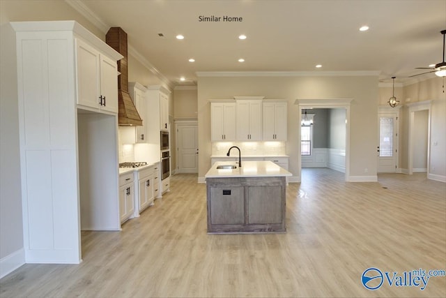 kitchen with white cabinetry, a kitchen island with sink, sink, and decorative backsplash