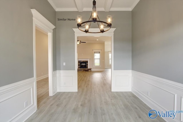 unfurnished dining area with crown molding, light hardwood / wood-style flooring, ceiling fan with notable chandelier, beam ceiling, and a stone fireplace