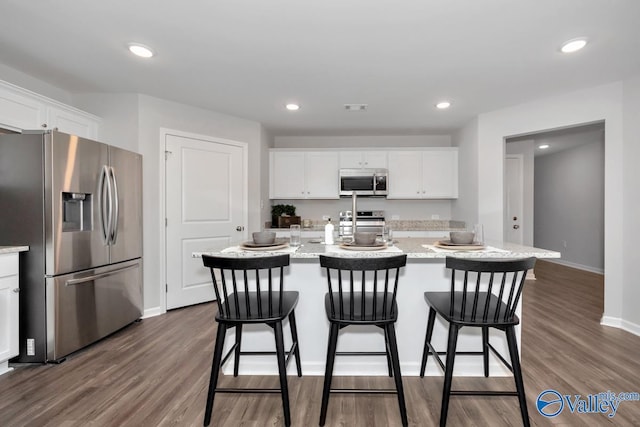 kitchen with white cabinetry, a center island with sink, dark hardwood / wood-style floors, stainless steel appliances, and light stone countertops