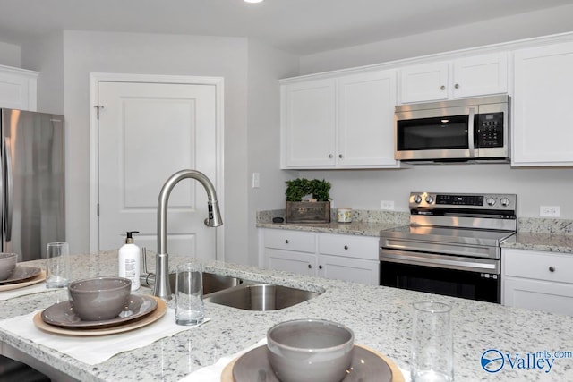 kitchen with white cabinetry, sink, light stone counters, and stainless steel appliances