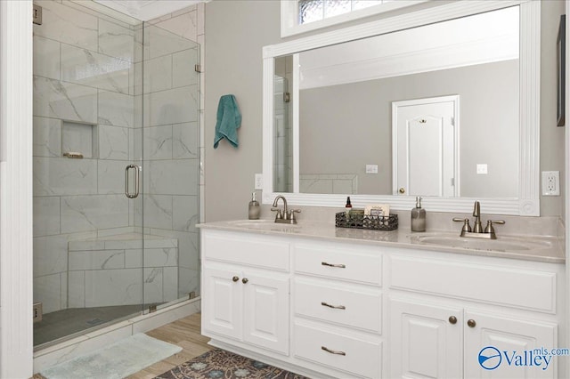 bathroom with a marble finish shower, a sink, double vanity, and wood finished floors