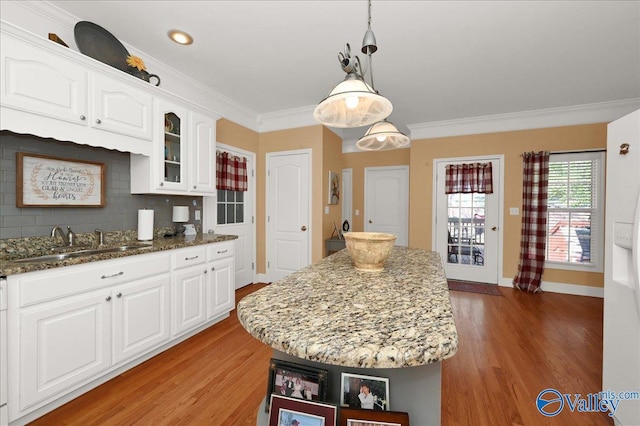 kitchen featuring white cabinets, glass insert cabinets, a sink, light wood-style floors, and stone countertops