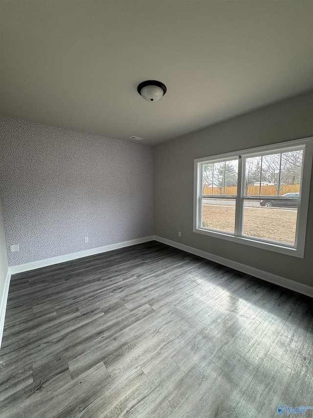 empty room featuring baseboards, light wood finished floors, visible vents, and wallpapered walls