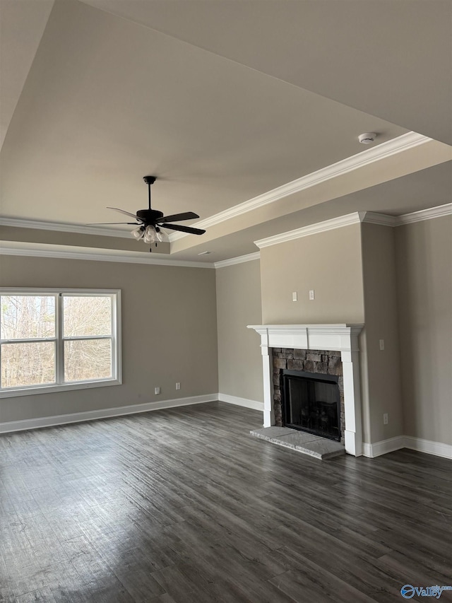 unfurnished living room featuring a raised ceiling, dark wood-type flooring, a ceiling fan, a stone fireplace, and baseboards