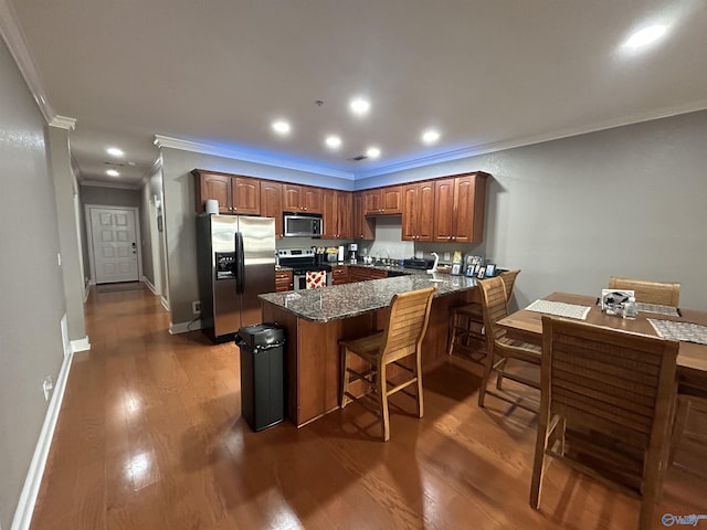 kitchen with a breakfast bar area, stainless steel appliances, a peninsula, dark wood-style flooring, and dark stone counters