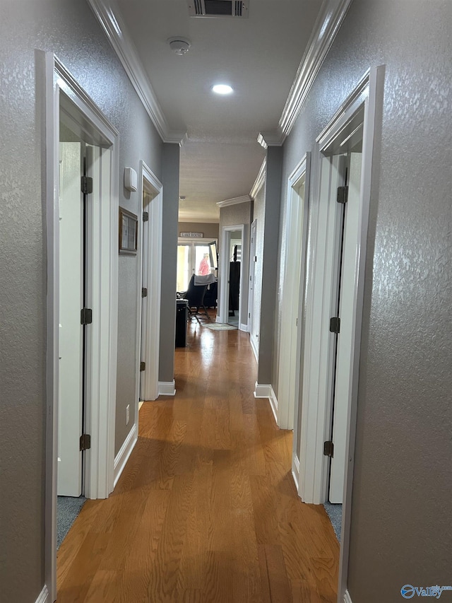 corridor featuring a textured wall, wood finished floors, visible vents, and crown molding