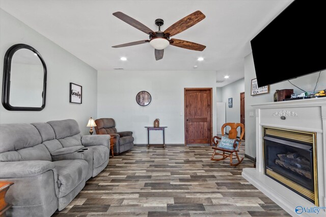 living area with baseboards, a glass covered fireplace, ceiling fan, wood finished floors, and recessed lighting