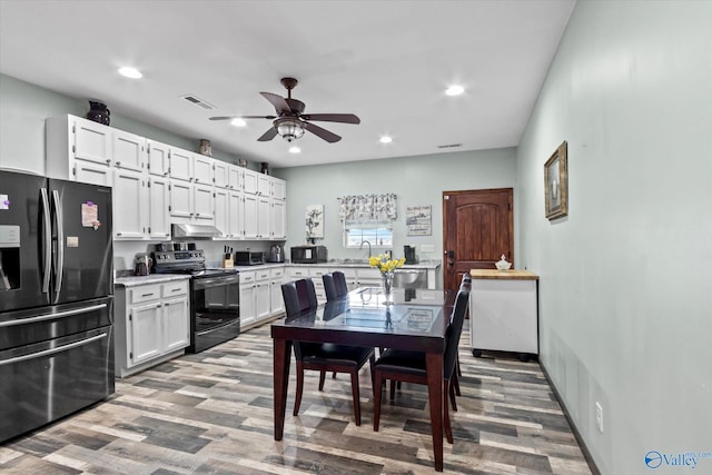 kitchen with light countertops, visible vents, white cabinets, under cabinet range hood, and black appliances