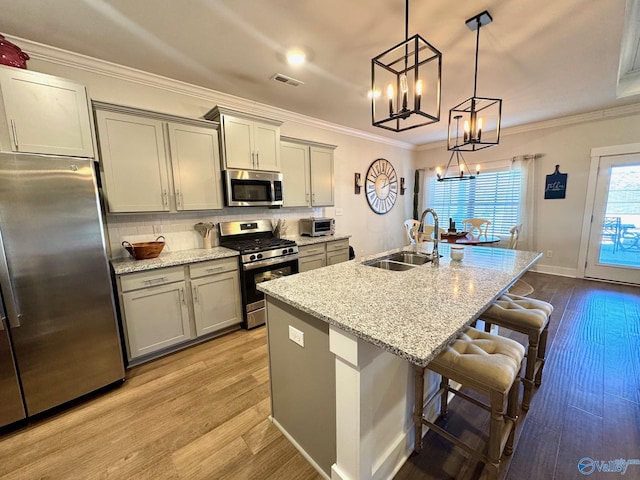 kitchen featuring wood finished floors, visible vents, a sink, stainless steel appliances, and crown molding