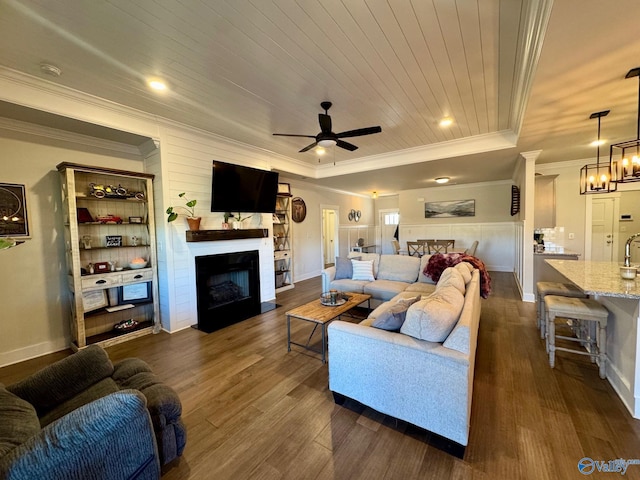 living area featuring a fireplace with flush hearth, ornamental molding, ceiling fan with notable chandelier, wooden ceiling, and dark wood-style floors