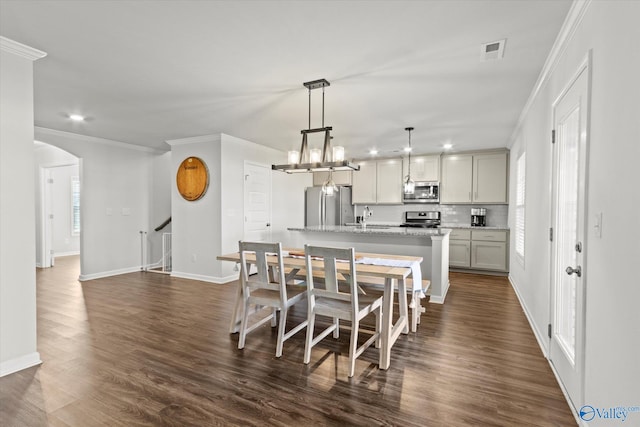 kitchen featuring a kitchen island with sink, a notable chandelier, crown molding, stainless steel appliances, and dark wood-type flooring