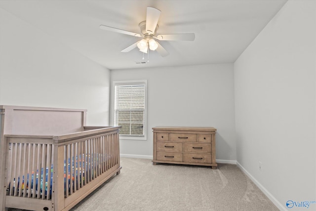 bedroom featuring a nursery area, ceiling fan, and light colored carpet