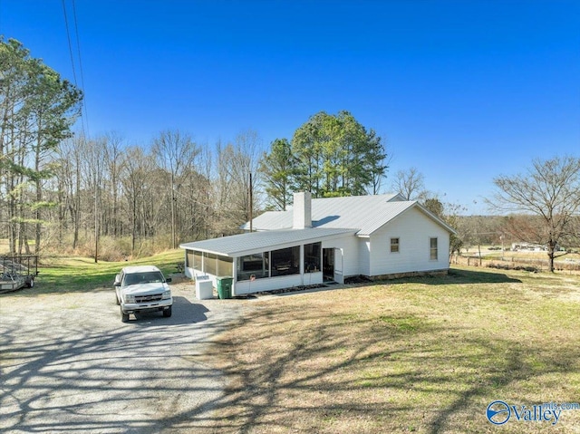 view of front of home with metal roof, a chimney, a front yard, and a sunroom