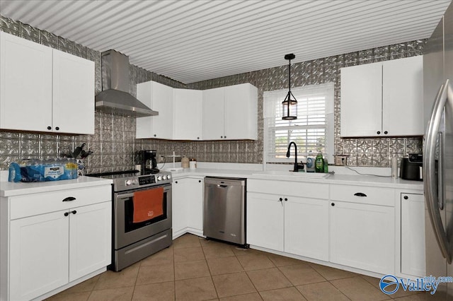 kitchen featuring decorative backsplash, appliances with stainless steel finishes, white cabinets, a sink, and wall chimney range hood