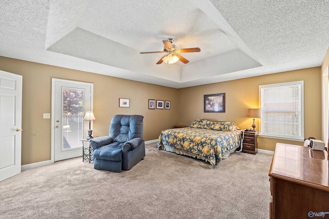 carpeted bedroom with multiple windows, access to exterior, a textured ceiling, and a tray ceiling