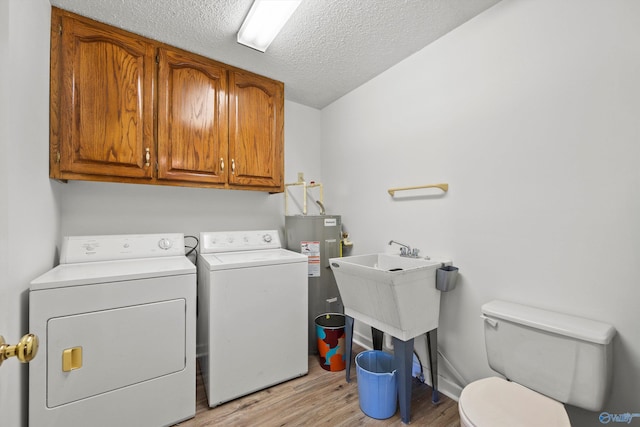 washroom featuring water heater, a textured ceiling, washing machine and clothes dryer, and light hardwood / wood-style floors