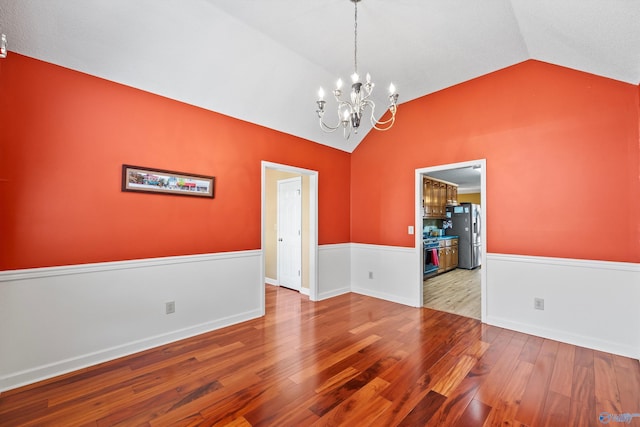 unfurnished room featuring an inviting chandelier, vaulted ceiling, and light hardwood / wood-style floors