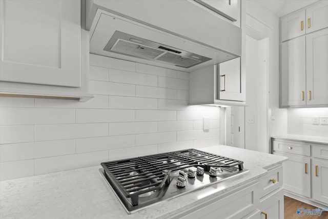 kitchen with decorative backsplash, light stone countertops, dark hardwood / wood-style flooring, stainless steel gas cooktop, and white cabinetry