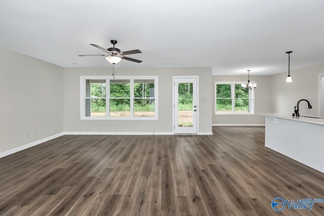 unfurnished living room with sink, a healthy amount of sunlight, ceiling fan with notable chandelier, and dark wood-type flooring