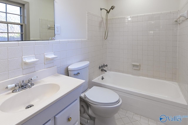 full bathroom featuring tile patterned floors, toilet, tiled shower / bath, tile walls, and vanity