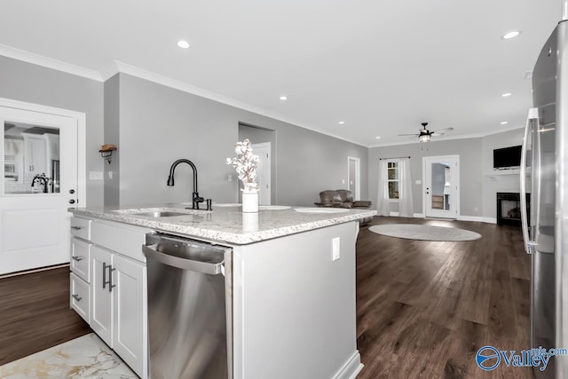 kitchen featuring a fireplace, a sink, white cabinets, open floor plan, and appliances with stainless steel finishes