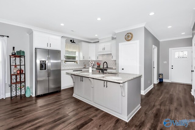 kitchen featuring light stone counters, an island with sink, white cabinets, and stainless steel fridge with ice dispenser