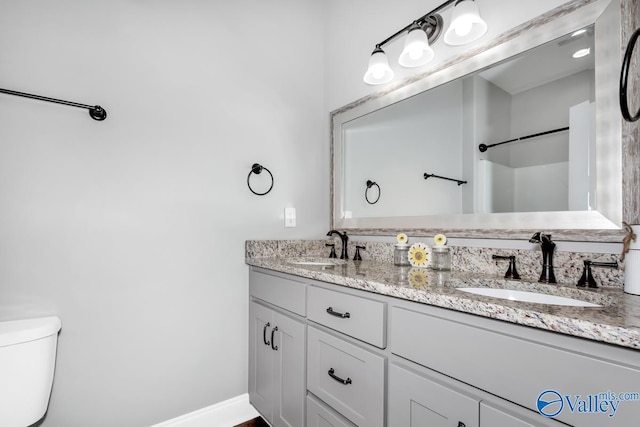 full bath featuring toilet, double vanity, baseboards, and a sink