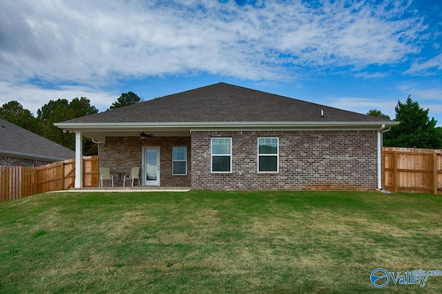 rear view of property with ceiling fan, a lawn, and brick siding