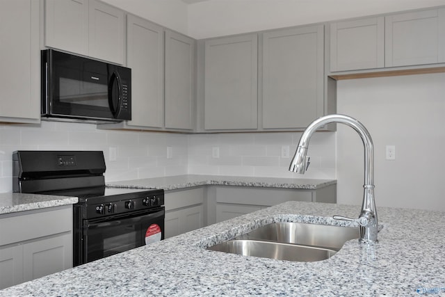 kitchen featuring sink, gray cabinetry, black appliances, light stone countertops, and decorative backsplash