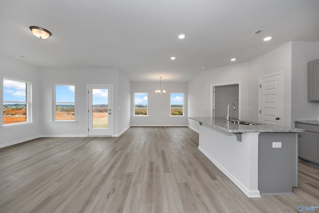 kitchen with sink, gray cabinetry, a center island with sink, light stone countertops, and light hardwood / wood-style floors