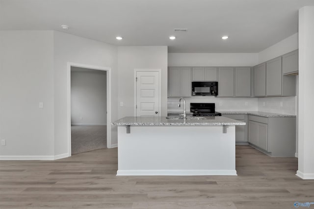 kitchen with gray cabinets, an island with sink, light stone countertops, and black appliances