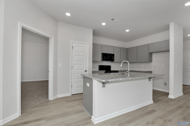 kitchen with stove, sink, light stone counters, and an island with sink