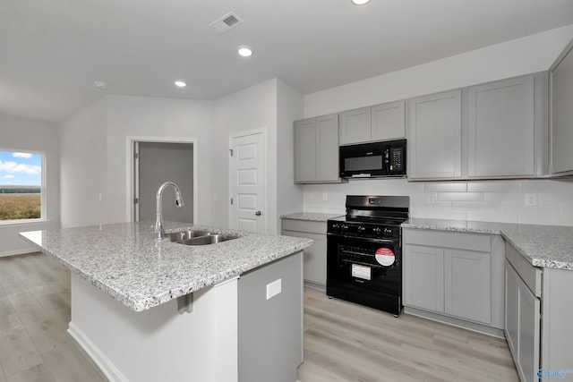 kitchen with gray cabinets, an island with sink, sink, backsplash, and black appliances