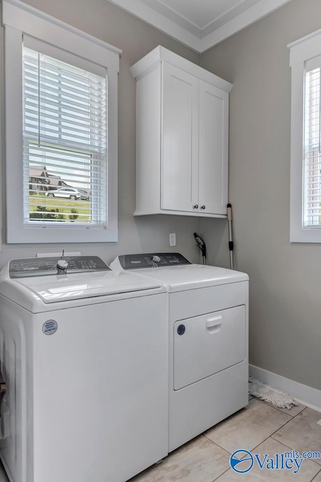 clothes washing area with cabinets, light tile patterned floors, crown molding, and washing machine and clothes dryer