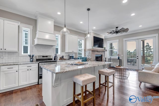 kitchen with custom range hood, dark hardwood / wood-style flooring, stainless steel range oven, decorative backsplash, and a fireplace