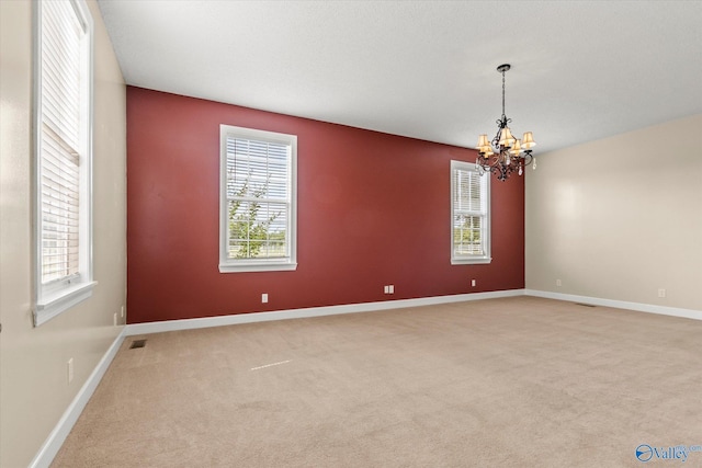 empty room featuring carpet, a healthy amount of sunlight, a notable chandelier, and baseboards