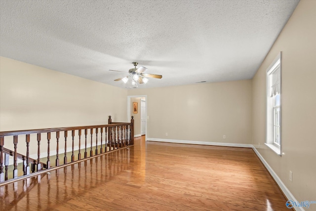 unfurnished room with a textured ceiling, wood finished floors, a ceiling fan, and baseboards