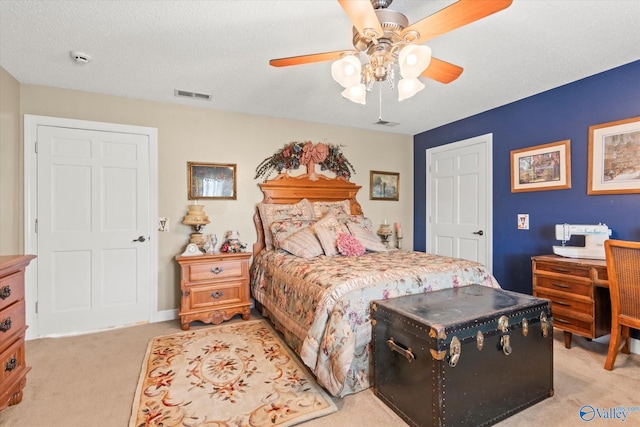 bedroom with a ceiling fan, visible vents, light carpet, and a textured ceiling