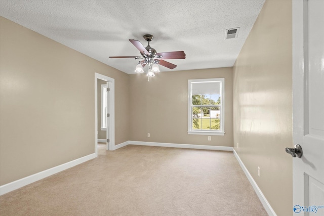 unfurnished room featuring a textured ceiling, light carpet, a ceiling fan, visible vents, and baseboards