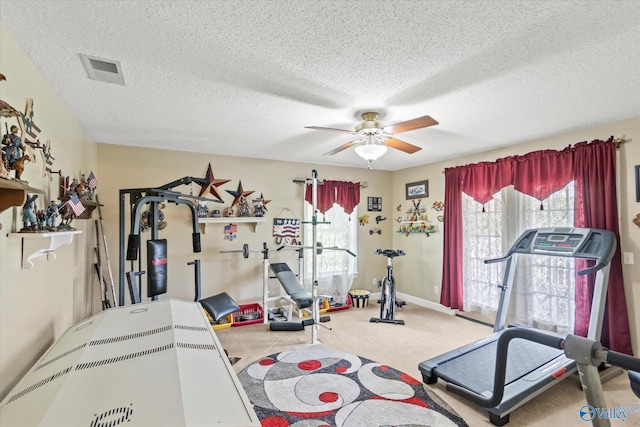 exercise area featuring visible vents, carpet flooring, ceiling fan, a textured ceiling, and baseboards